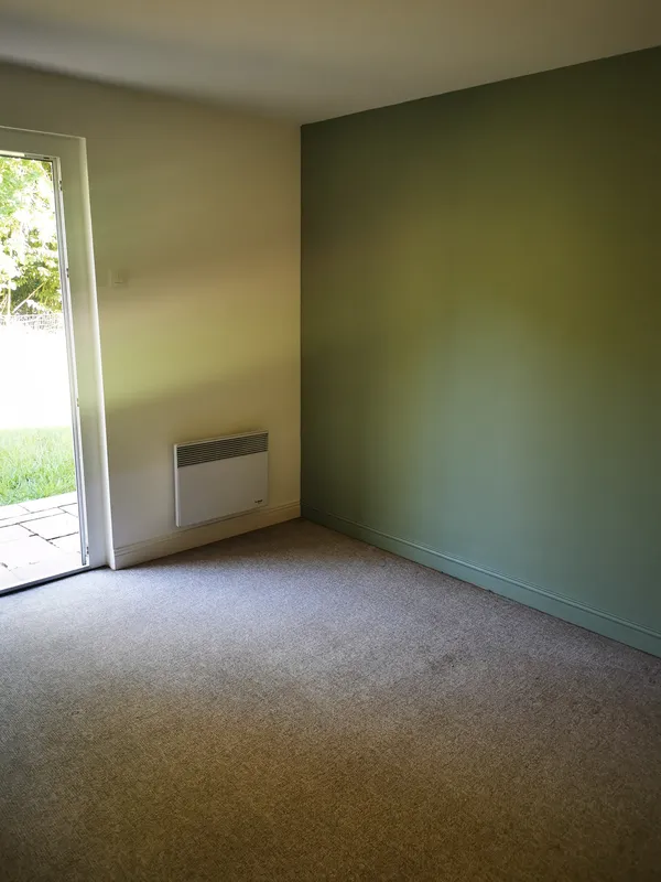 Chambre avec moquette beige nettoyée, mur vert sauge et porte-fenêtre sur jardin — Mios, mai 2026