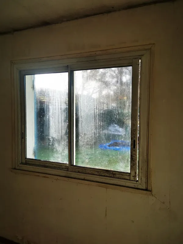 Fenêtre coulissante encrassée avec coulures et vitres souillées, murs noircis — Léognan 2025